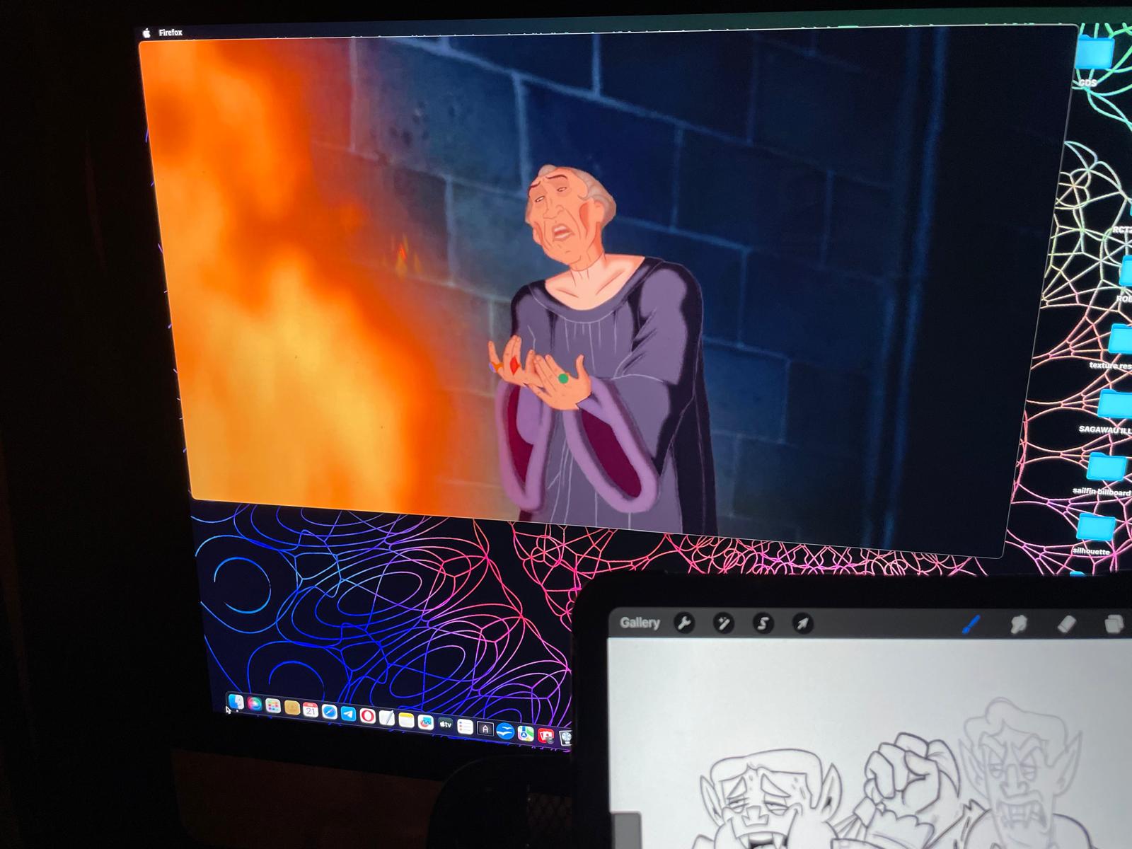 A phone photo of a desktop monitor playing The Hunchback of Notre Dame, with a KNM character sketch open in Procreate on a tablet in the foreground