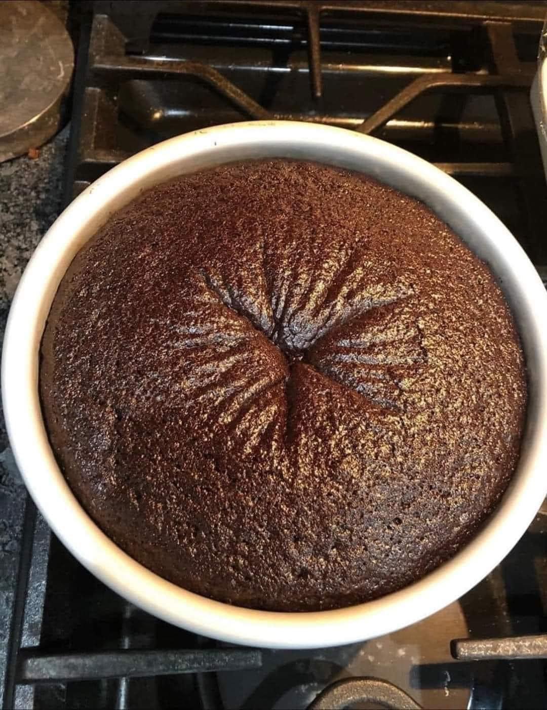 An overhead photo of a cracked, dome-topped chocolate cake baking in a pan on the stove