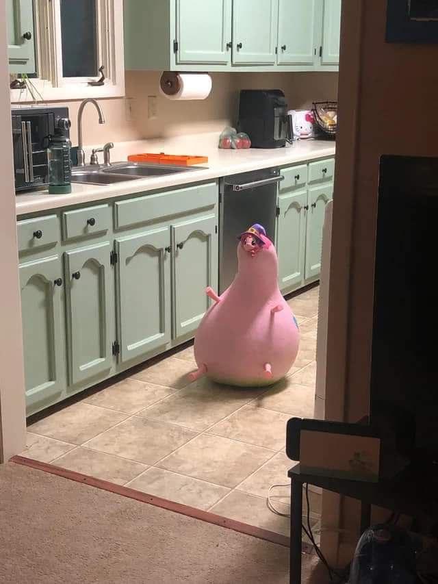 A large, deflating pink pig-shaped pool float slumped over on a kitchen floor
